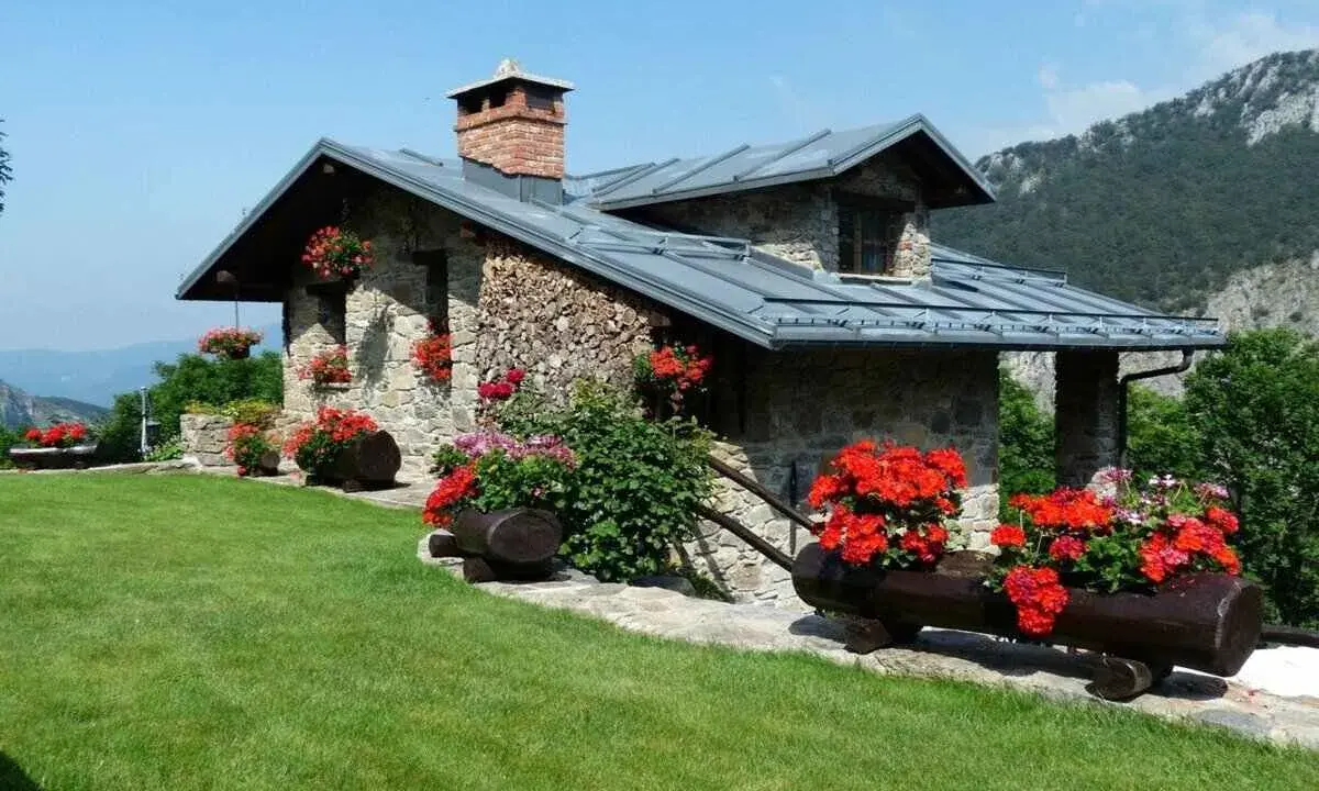 Charmante maison en pierre avec cheminée, entourée de fleurs rouges. Idéale pour ma prime rénov résidence secondaire.