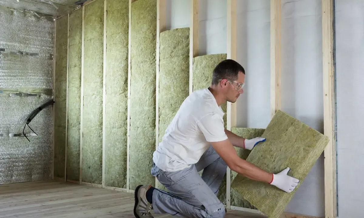Un ouvrier installe un isolant minéral dans un mur en bois. Un bon **prix isolation** pour un confort thermique optimal.