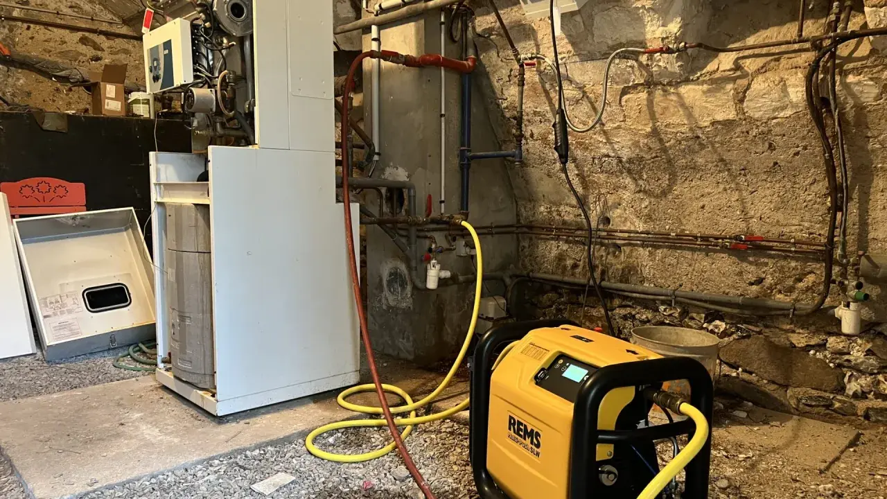 Un technicien effectue le desembouage d'une pompe à chaleur dans une chaufferie. L'équipement est relié à la chaudière par des tuyaux jaunes.