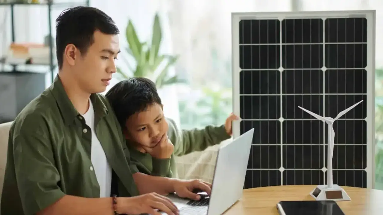 Père et fils étudient l'énergie solaire et éolienne sur un ordinateur portable, un panneau solaire et une éolienne à proximité. Un projet d'installation cacsi sans consuel.