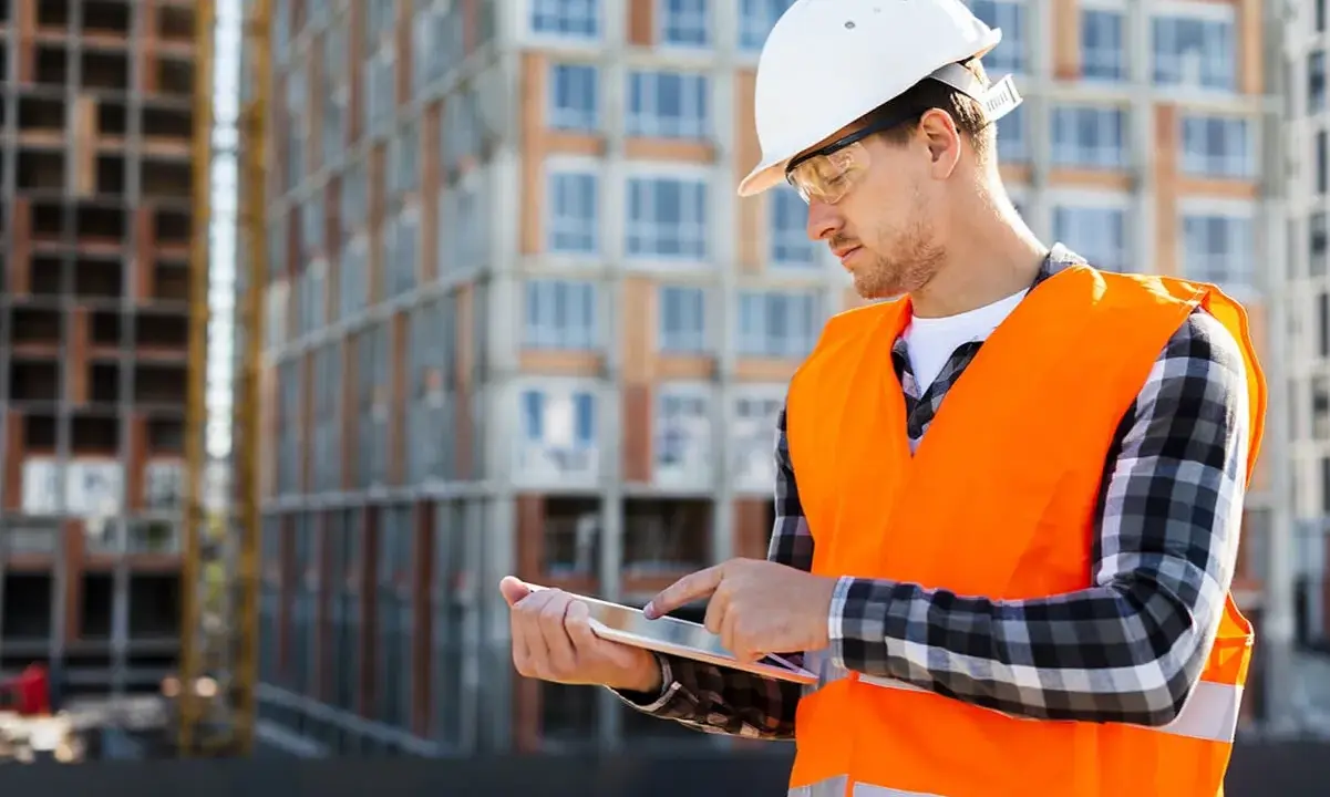 Ingénieur consultant un plan sur tablette devant un immeuble en construction.