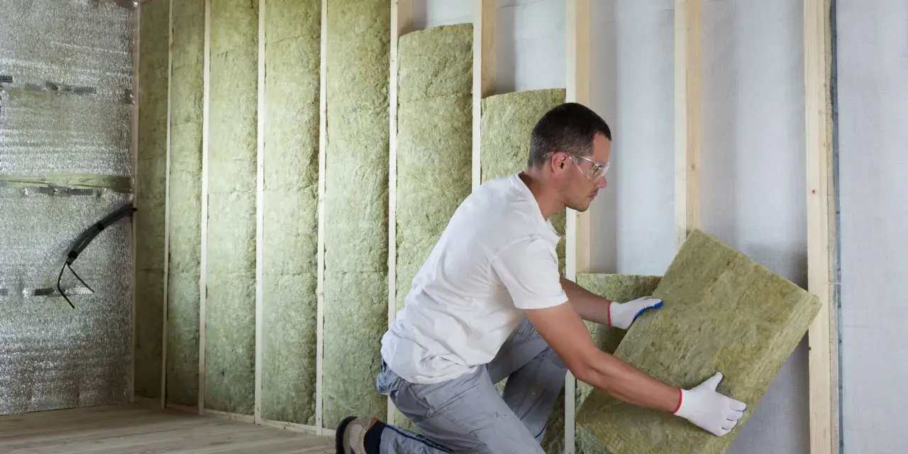 Un ouvrier installe des panneaux d'isolant dans un mur en bois. Il est important de connaître le prix au m2 pour l'isolation intérieure afin de maîtriser son budget travaux.