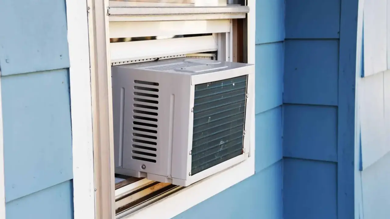 Climatisation réversible sans groupe extérieur installée dans une fenêtre. L'unité blanche est visible sur un mur bleu.