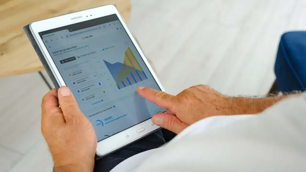 Homme consultant sa tablette : suivi de production solaire, consommation, autoconsommation et injection gratuite ENEDIS.