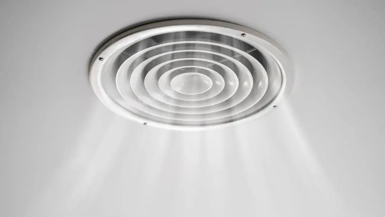 Grille de ventilation ronde au plafond, diffusant une légère brume. On dirait que la VMC pas assez puissante peine à renouveler l'air.