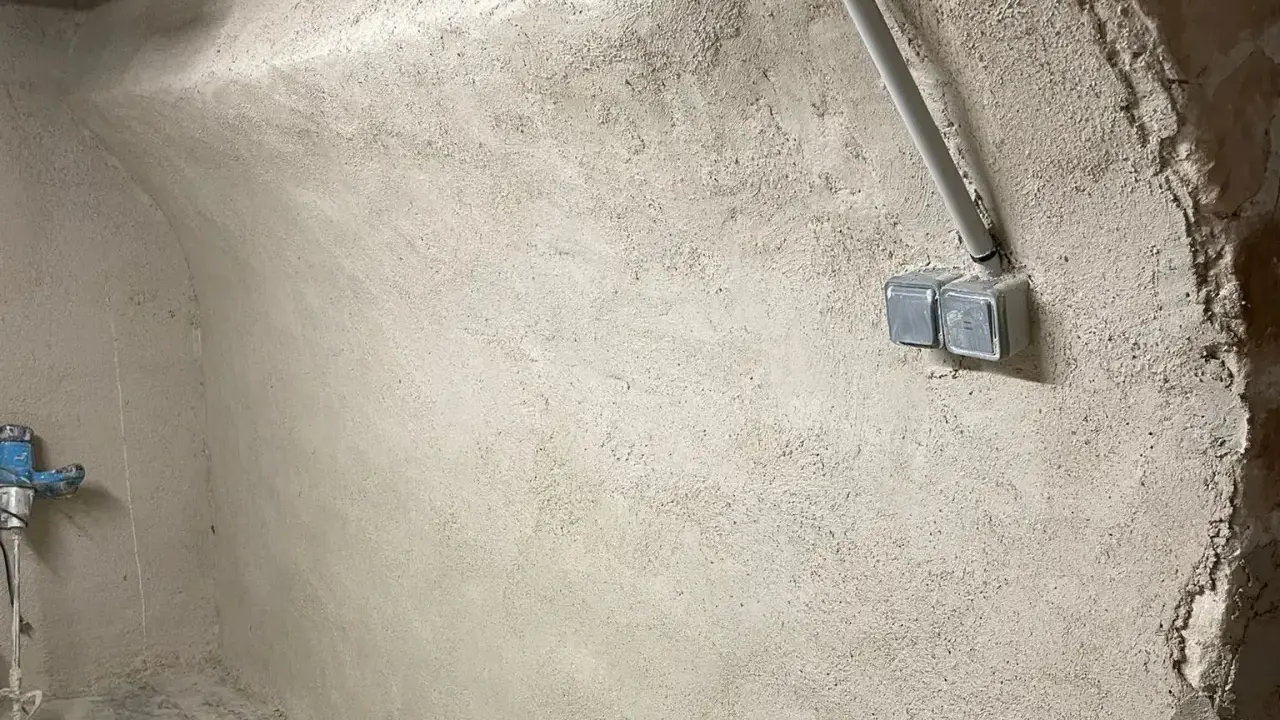 Mur brut avec prises électriques et tuyau, prêt pour enlever humidité maison. Un robinet bleu est visible à gauche.