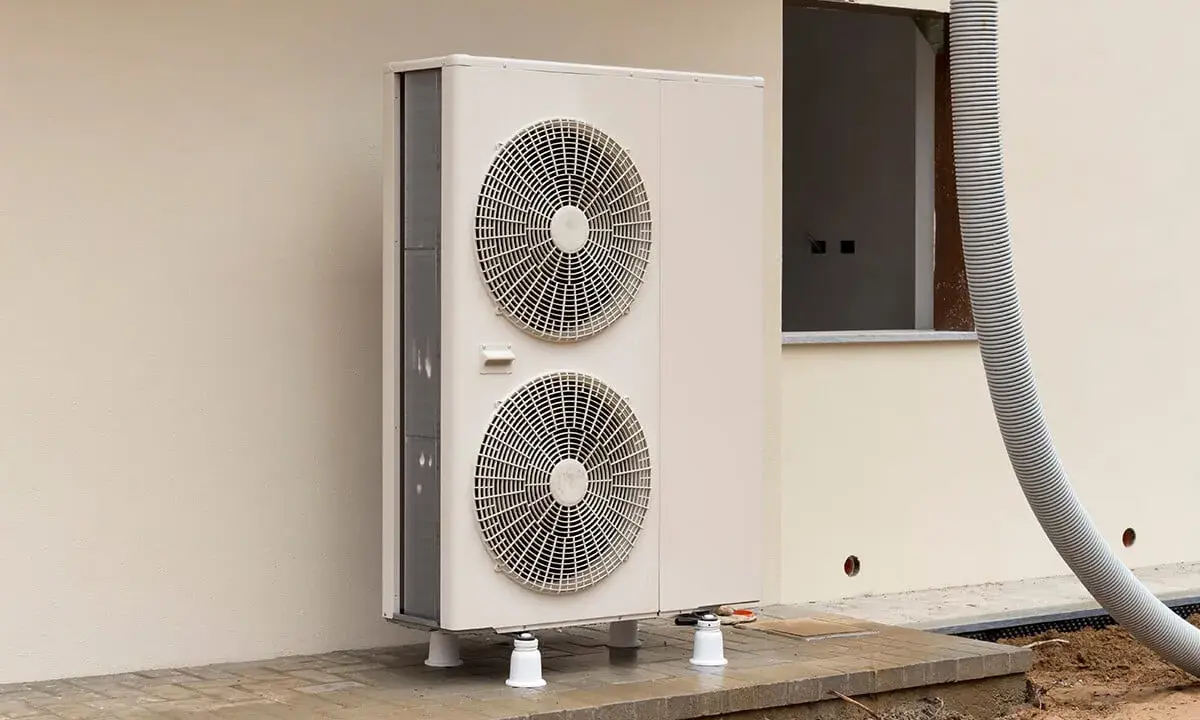 Une pompe à chaleur monobloc, avec ses deux ventilateurs, est installée à l'extérieur d'un bâtiment en construction.