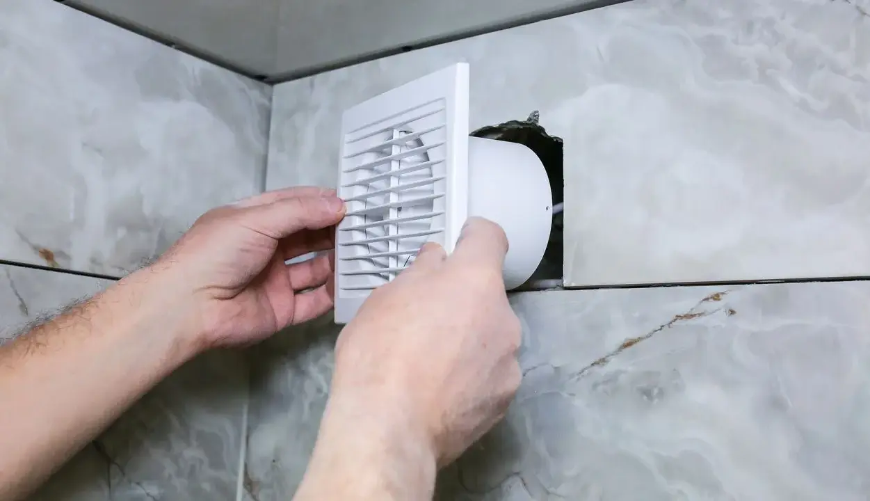 Installation d'une grille de ventilation VMC pour lutter contre la condensation dans une salle de bain carrelée.