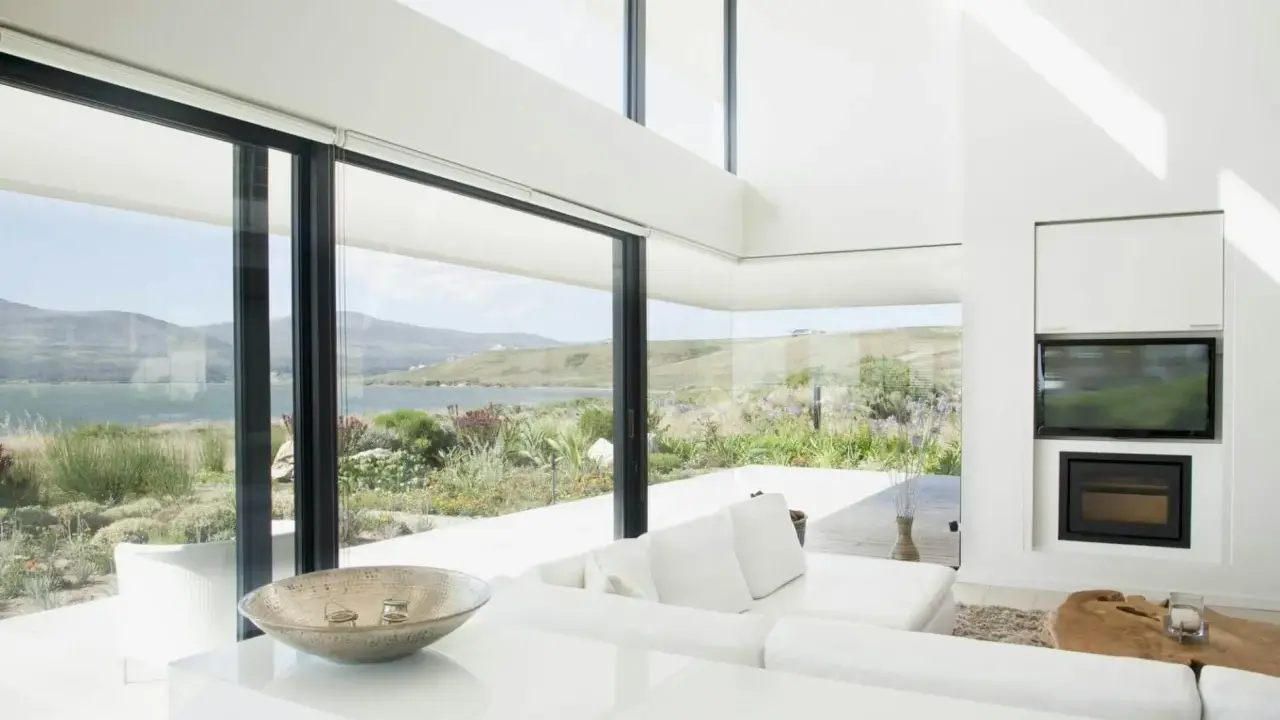 Salon moderne avec vue panoramique sur la mer, baigné de lumière grâce à d'immenses fenêtres en triple vitrage.