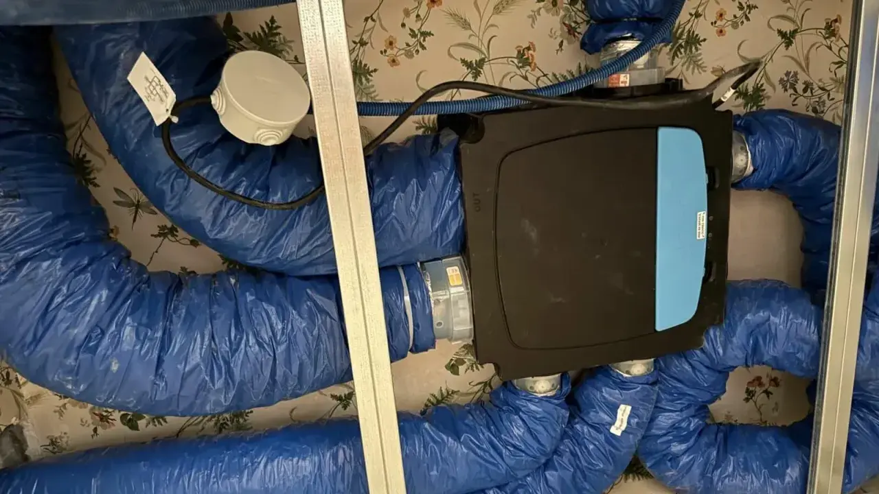 Système de ventilation centralisé avec un boîtier noir et bleu, entouré de conduits bleus isolés. Ce système VMC programmable assure un air sain.