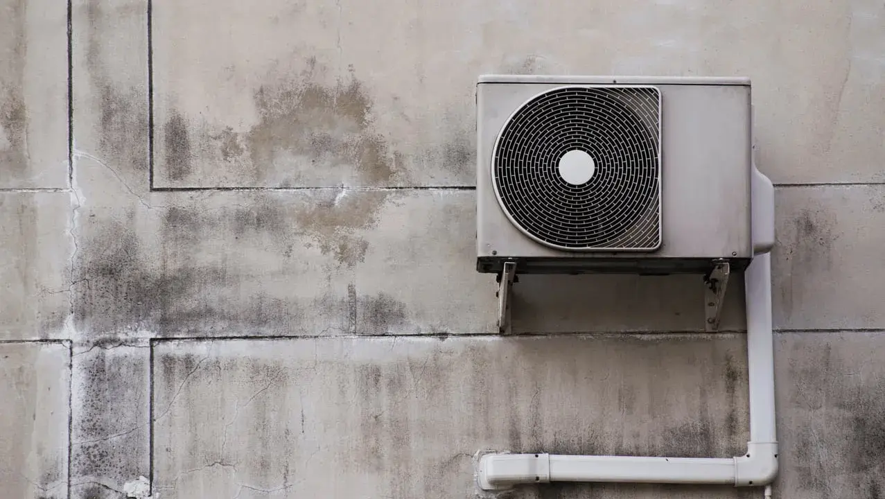 Unité extérieure de pompe à chaleur, sale et fissurée sur un mur décrépi. Avis négatif sur ce système.