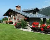 Charmante maison en pierre avec cheminée, entourée de fleurs rouges. Idéale pour ma prime rénov résidence secondaire.