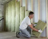 Un ouvrier installe un isolant minéral dans un mur en bois. Un bon **prix isolation** pour un confort thermique optimal.