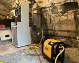 Un technicien effectue le desembouage d'une pompe à chaleur dans une chaufferie. L'équipement est relié à la chaudière par des tuyaux jaunes.