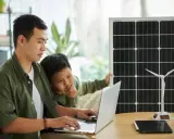Père et fils étudient l'énergie solaire et éolienne sur un ordinateur portable, un panneau solaire et une éolienne à proximité. Un projet d'installation cacsi sans consuel.