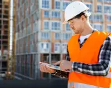 Ingénieur consultant un plan sur tablette devant un immeuble en construction.