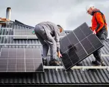 Deux ouvriers installent un panneau solaire sur un toit. La dimension du panneau solaire est adaptée pour maximiser la capture d'énergie.