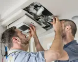 Deux hommes installent un système VMC dans un faux plafond. C'est là où se trouve la VMC dans une maison.