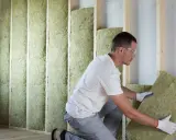 Un ouvrier installe des panneaux d'isolant dans un mur en bois. Il est important de connaître le prix au m2 pour l'isolation intérieure afin de maîtriser son budget travaux.