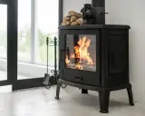 Un feu crépite dans ce cee poele a bois noir, prêt à réchauffer la pièce. Des bûches attendent sur le dessus.