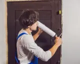 Un homme en salopette bleue utilise une mousse expansive pour comment isoler une porte.
