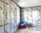 Intérieur en cours d'isolation, murs recouverts de pare-vapeur Isover Vario Xtra. Rouleaux de tuyaux bleus et rouges au sol. Un coup de pouce pour une isolation performante.