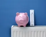 Tirelire rose sur un radiateur blanc, à côté d'un thermomètre. Pensez à l'entretien chaudière déductible impôts pour faire des économies.