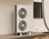 Une pompe à chaleur monobloc, avec ses deux ventilateurs, est installée à l'extérieur d'un bâtiment en construction.
