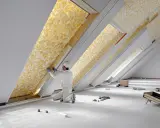 Un ouvrier installe un matériau isolant jaune texturé dans un grenier, assurant le meilleur isolant thermique pour la maison.