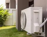 Unité extérieure de pompe à chaleur avec tuyau pour l'évacuation eau condensation. L'appareil est fixé au mur d'une maison, près d'une pelouse et de végétation.