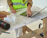 Architectes discutent des plans, pointant du doigt l'emplacement idéal pour installer la VMC dans le modèle de maison.