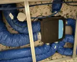 Système de ventilation centralisé avec un boîtier noir et bleu, entouré de conduits bleus isolés. Ce système VMC programmable assure un air sain.
