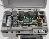 Intérieur d'un boîtier gris ouvert, révélant un circuit imprimé VMC, une batterie et des fils. Le VMC qui bip pourrait indiquer un problème.