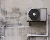 Unité extérieure de pompe à chaleur, sale et fissurée sur un mur décrépi. Avis négatif sur ce système.