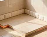 Coupe d'un sol carrelé montrant le système de chauffage et l'isolation sous carrelage, avec des matériaux isolants moelleux sur les côtés.