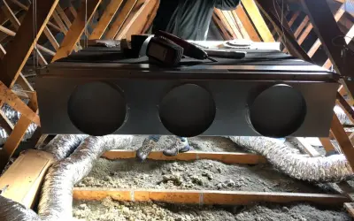 Installation d'un système de climatisation gainable dans un grenier. Un technicien est visible, prêt pour l'entretien.