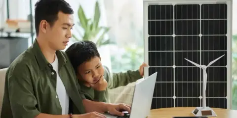 Père et fils étudient l'énergie solaire et éolienne sur un ordinateur portable, un panneau solaire et une éolienne à proximité. Un projet d'installation cacsi sans consuel.