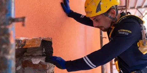 Un ouvrier en casque jaune effectue des travaux d'isolation extérieur, appliquant un enduit sur un mur orange.