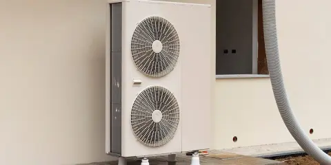 Une pompe à chaleur monobloc, avec ses deux ventilateurs, est installée à l'extérieur d'un bâtiment en construction.