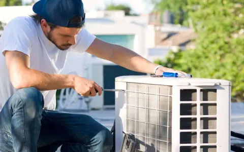 Un technicien effectue l'entretien d'une pompe à chaleur sur un toit, utilisant un tournevis pour ajuster l'unité extérieure.