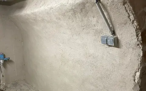 Mur brut avec prises électriques et tuyau, prêt pour enlever humidité maison. Un robinet bleu est visible à gauche.