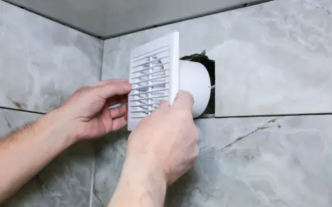 Installation d'une grille de ventilation VMC pour lutter contre la condensation dans une salle de bain carrelée.