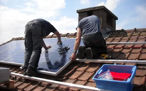 Deux ouvriers installent des panneaux solaires sur un toit. Une demande de travaux panneau solaire est en cours.
