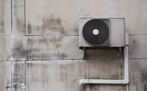 Unité extérieure de pompe à chaleur, sale et fissurée sur un mur décrépi. Avis négatif sur ce système.