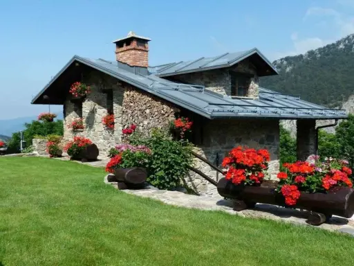 Charmante maison en pierre avec cheminée, entourée de fleurs rouges. Idéale pour ma prime rénov résidence secondaire.