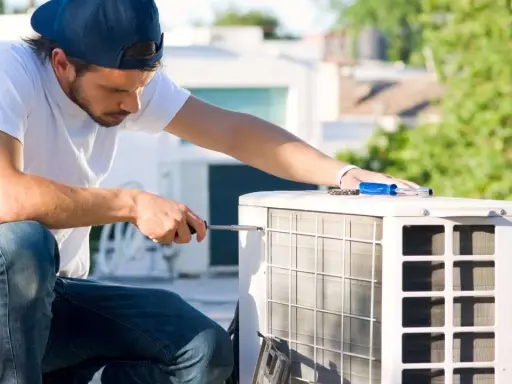 Un technicien effectue l'entretien d'une pompe à chaleur sur un toit, utilisant un tournevis pour ajuster l'unité extérieure.