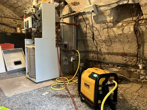 Un technicien effectue le desembouage d'une pompe à chaleur dans une chaufferie. L'équipement est relié à la chaudière par des tuyaux jaunes.