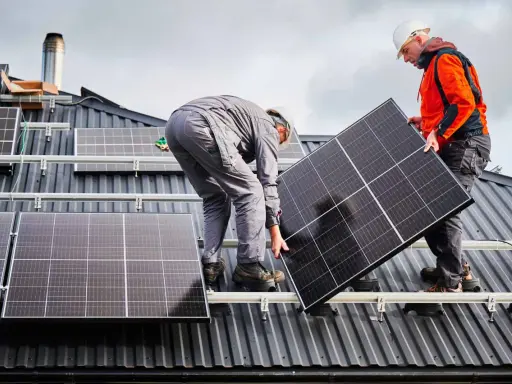 Deux ouvriers installent un panneau solaire sur un toit. La dimension du panneau solaire est adaptée pour maximiser la capture d'énergie.