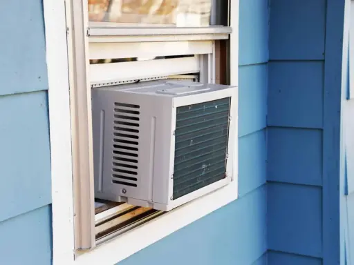 Climatisation réversible sans groupe extérieur installée dans une fenêtre. L'unité blanche est visible sur un mur bleu.