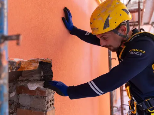 Un ouvrier en casque jaune effectue des travaux d'isolation extérieur, appliquant un enduit sur un mur orange.